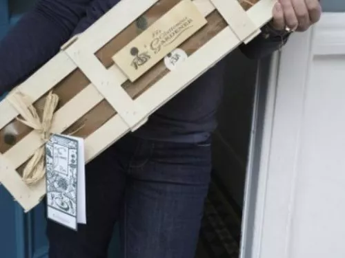 A wooden gift crate with a gift tag held by two hands.