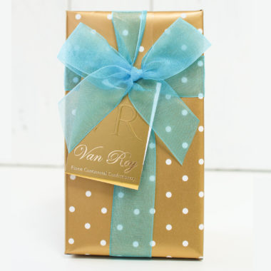 A beautifully wrapped chocolate box in gold and white polka dot gift wrap with a sheer bright blue Chiffon ribbon and a golden product tag.