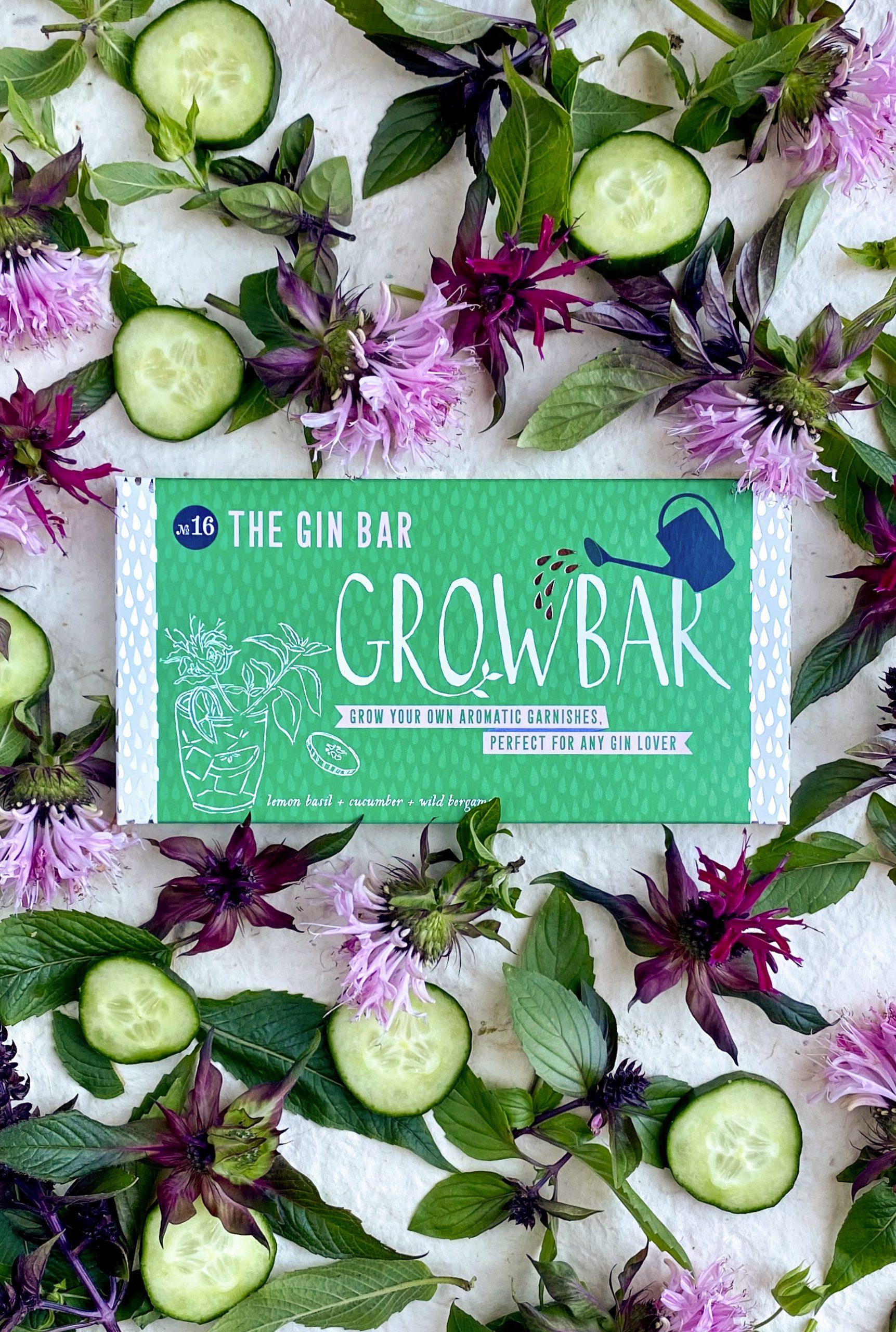 A green gin grow bar surrounded by slices of cucumber, leaves of lemon basil and purple wild bergamot flowers.