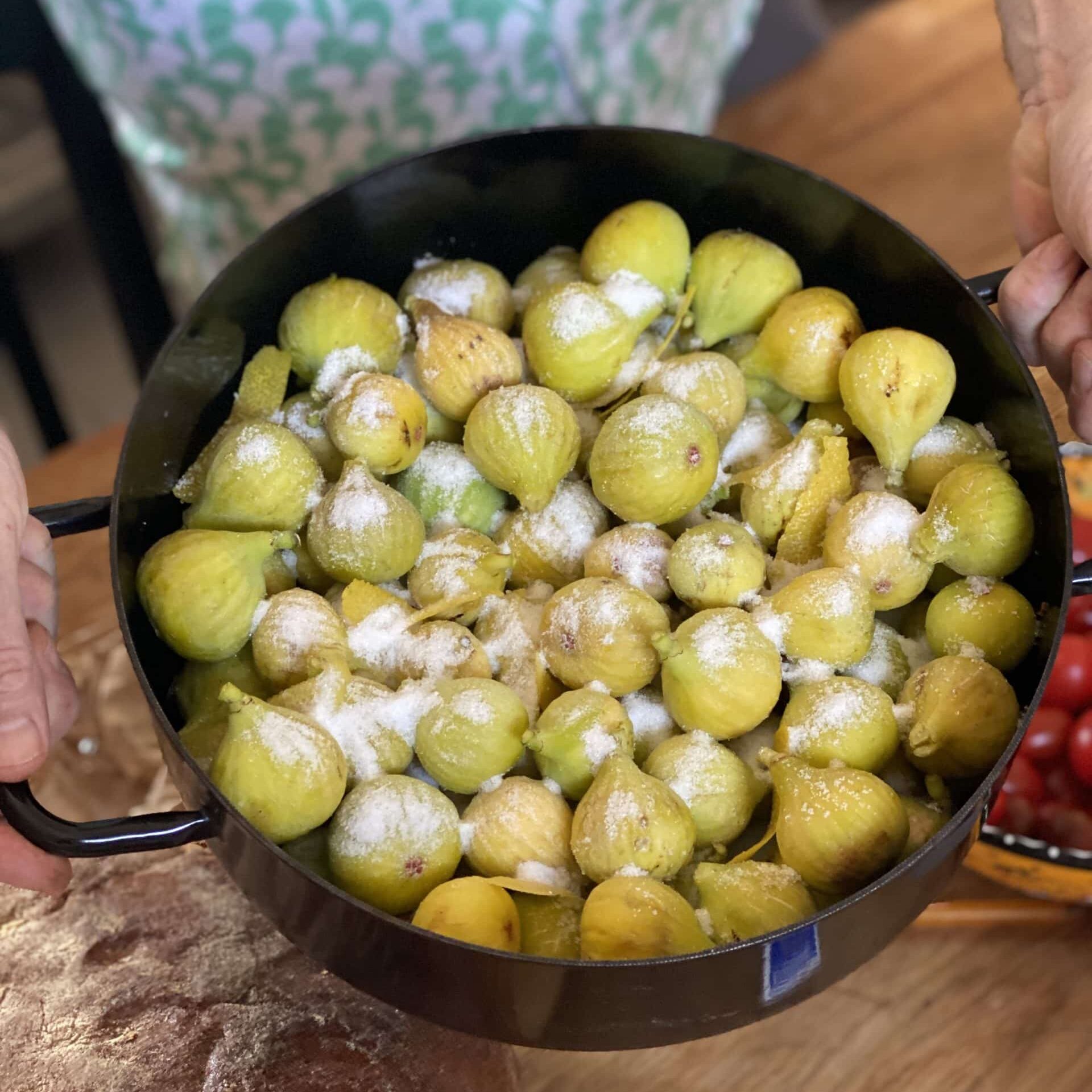 Pan of small green figs with a dusting of sugar being held by two hands.