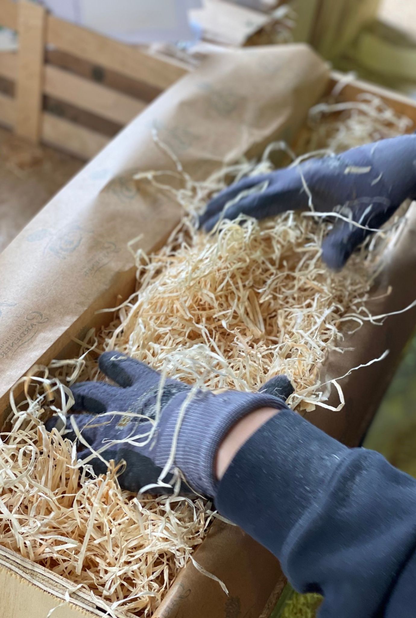 Two gloved hands packing straw into a wooden crate.