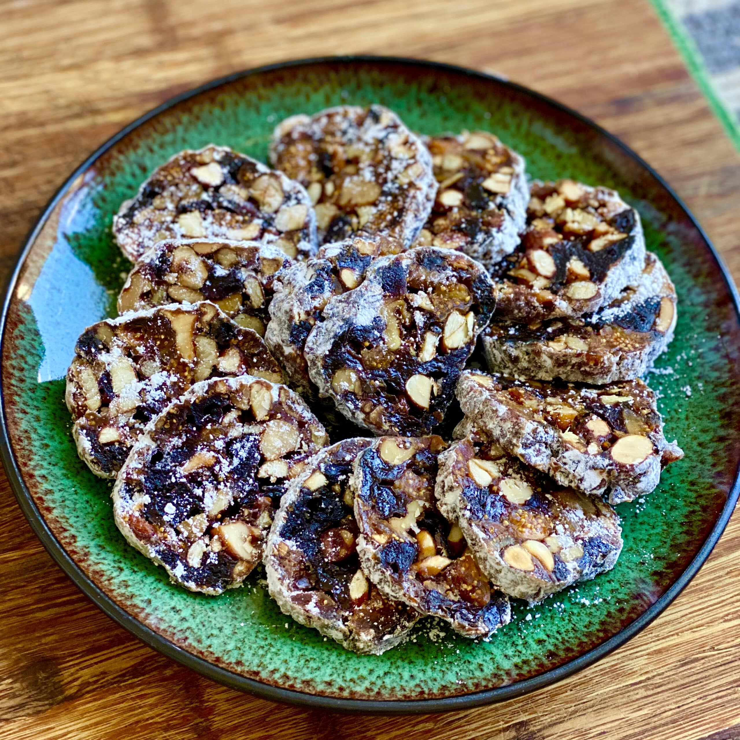 Sliced panforte cake with dried fruits, chopped nuts and icing sugar placed on a green plate.