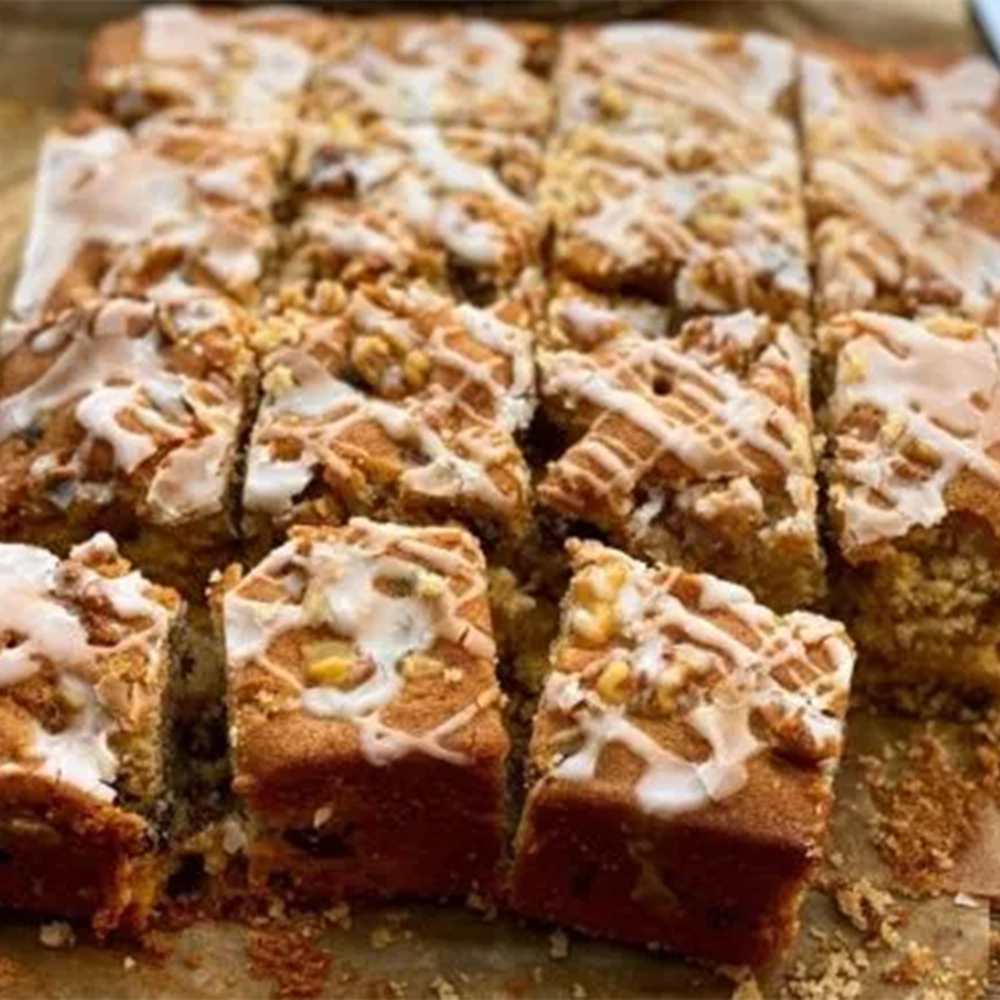 Large cake squares of a mulled cider and walnut cake with chopped walnuts topping and sugar icing on baking paper with a knife.