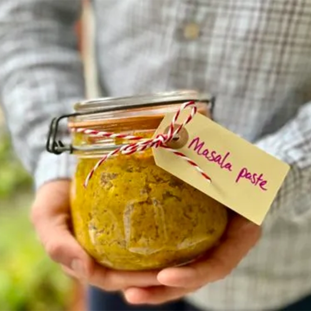 A canning jar with a beige - yellow Masala paste and a description tag held by two hands.