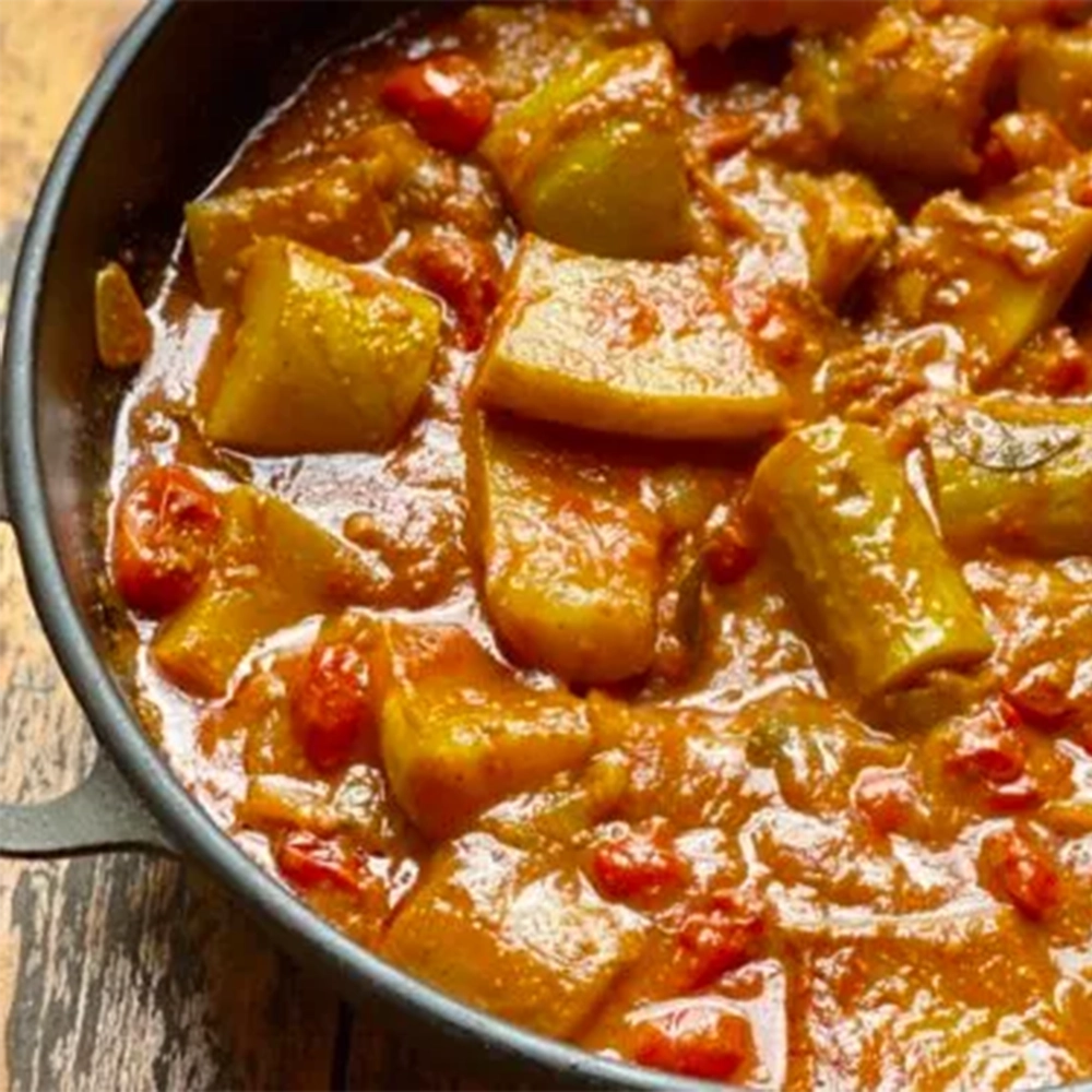 A cast iron pot filled with a Tromboncino masala meal with tromboncino squash, garlic and baby tomatoes in an orange coloured curry sauce.