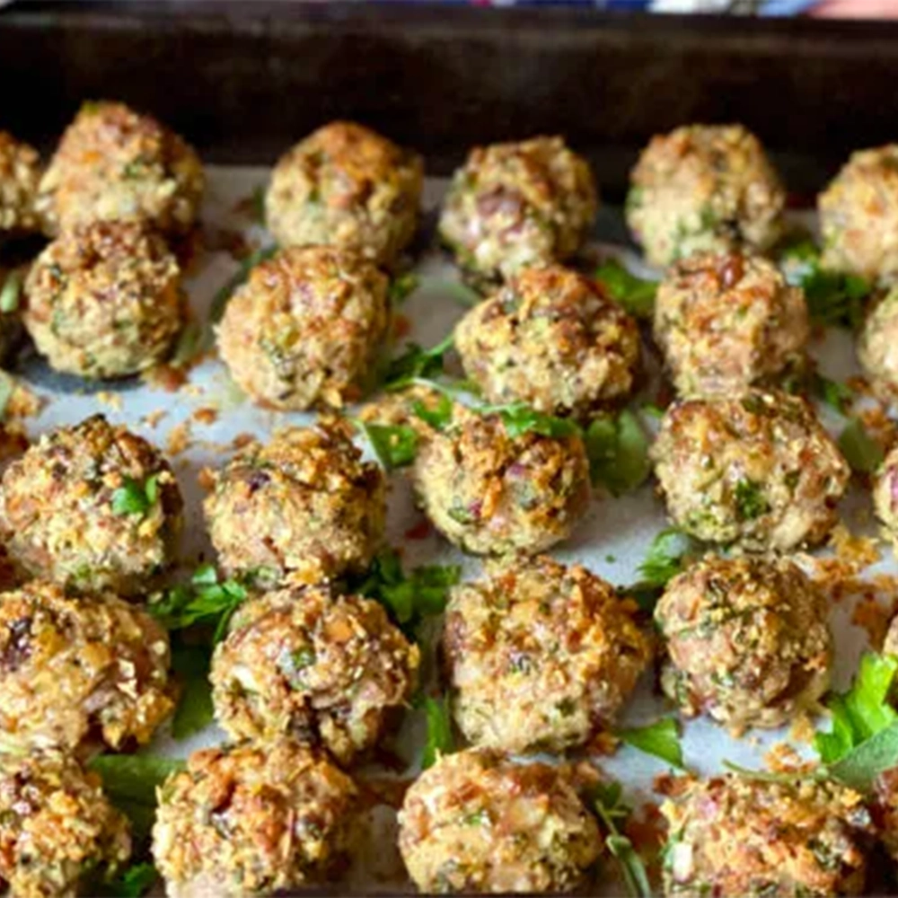 A tray with small Christmas stuffing balls made of chestnuts, breadcrumbs, parsley, sage, rosemary, thyme with fresh herbs sprinkled on top.