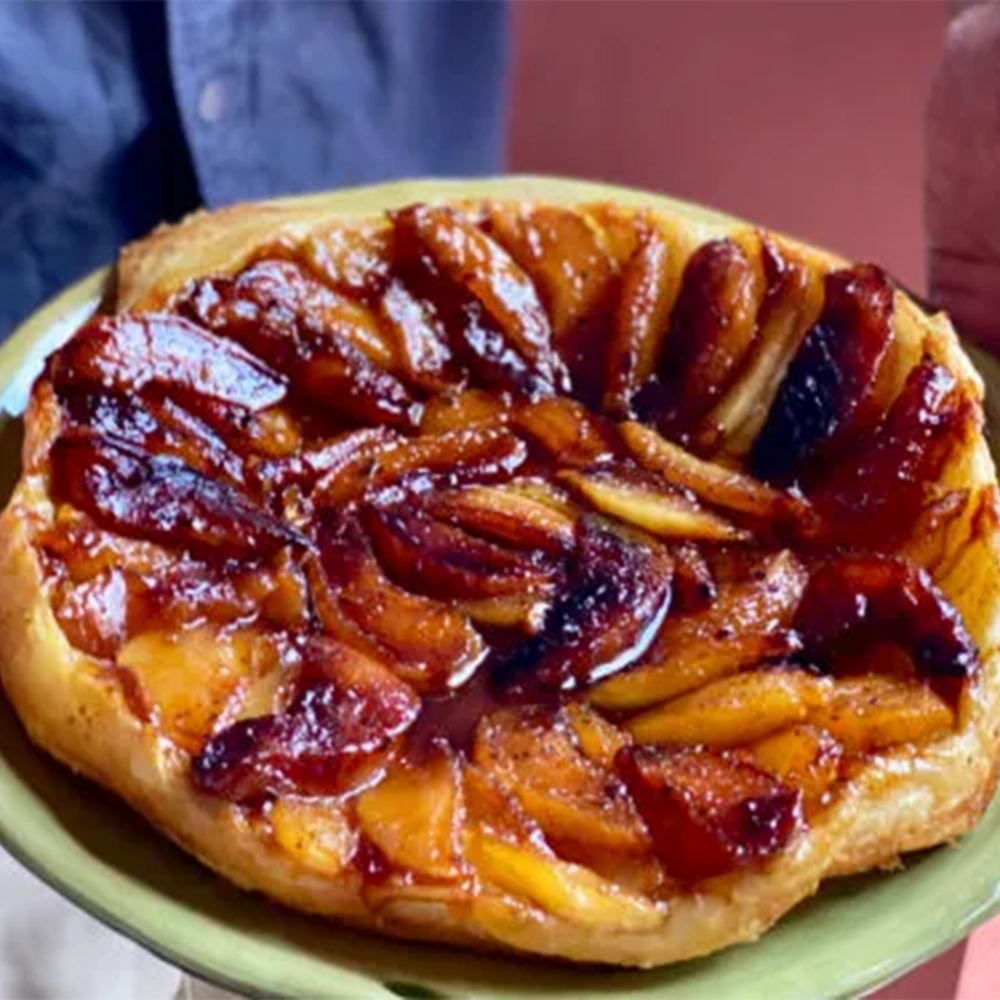 An Apple and Thai Lime Tarte Tatin with quartered caramelised apples on a puffy pastry served on a green plate held by two hands.