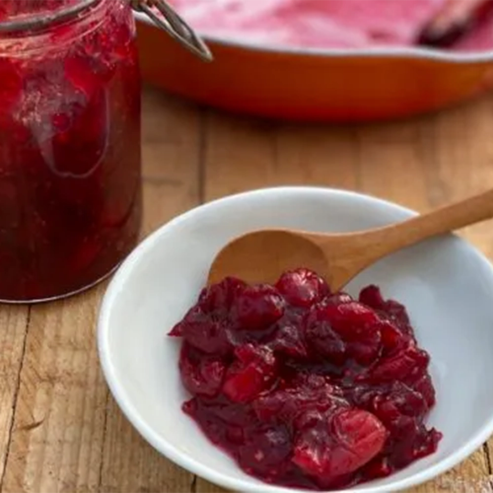 a small white dish on a wooden table with a red spiced cranberry and calamondin orange compote.