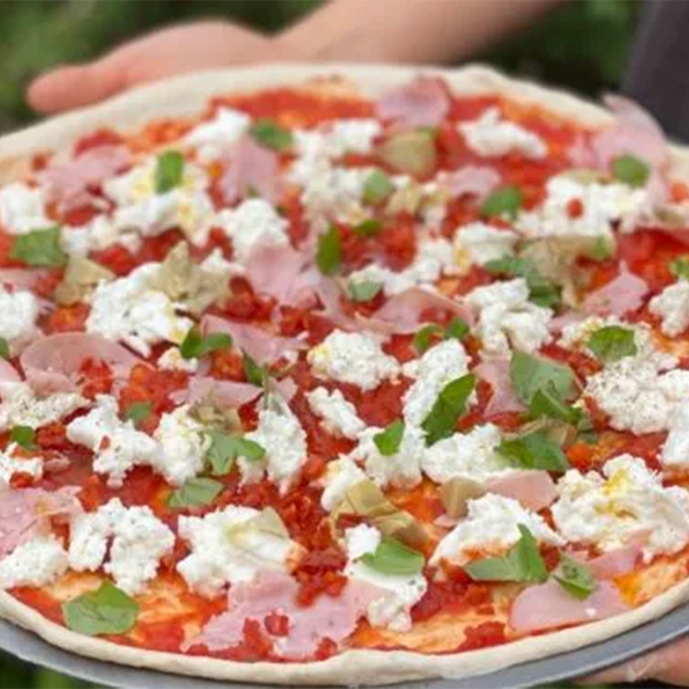 A large plate with an Italian Mozzarella and Ham pizza with tomato sauce and fresh basil, held by two hands.