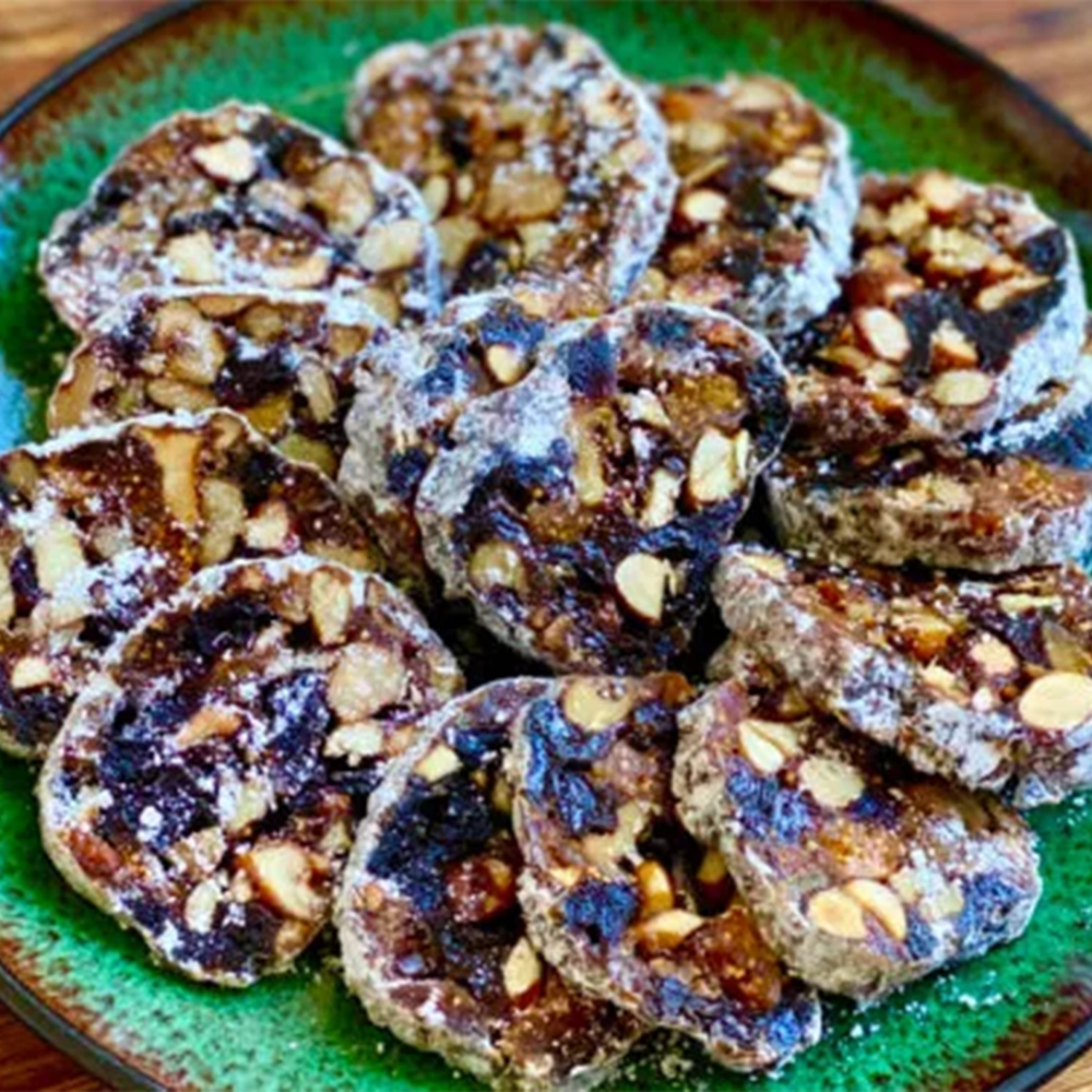 Sliced panforte cake with dried fruits, chopped nuts and icing sugar placed on a green plate.