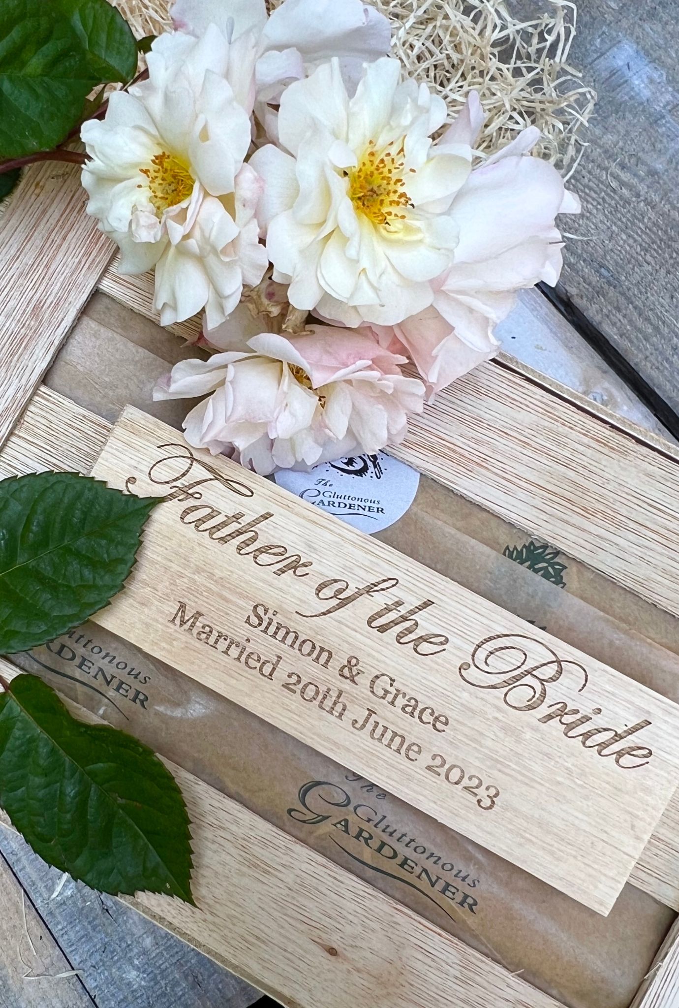 Close up of personalised Father of the Bride wooden plaque on crate with white flowers.