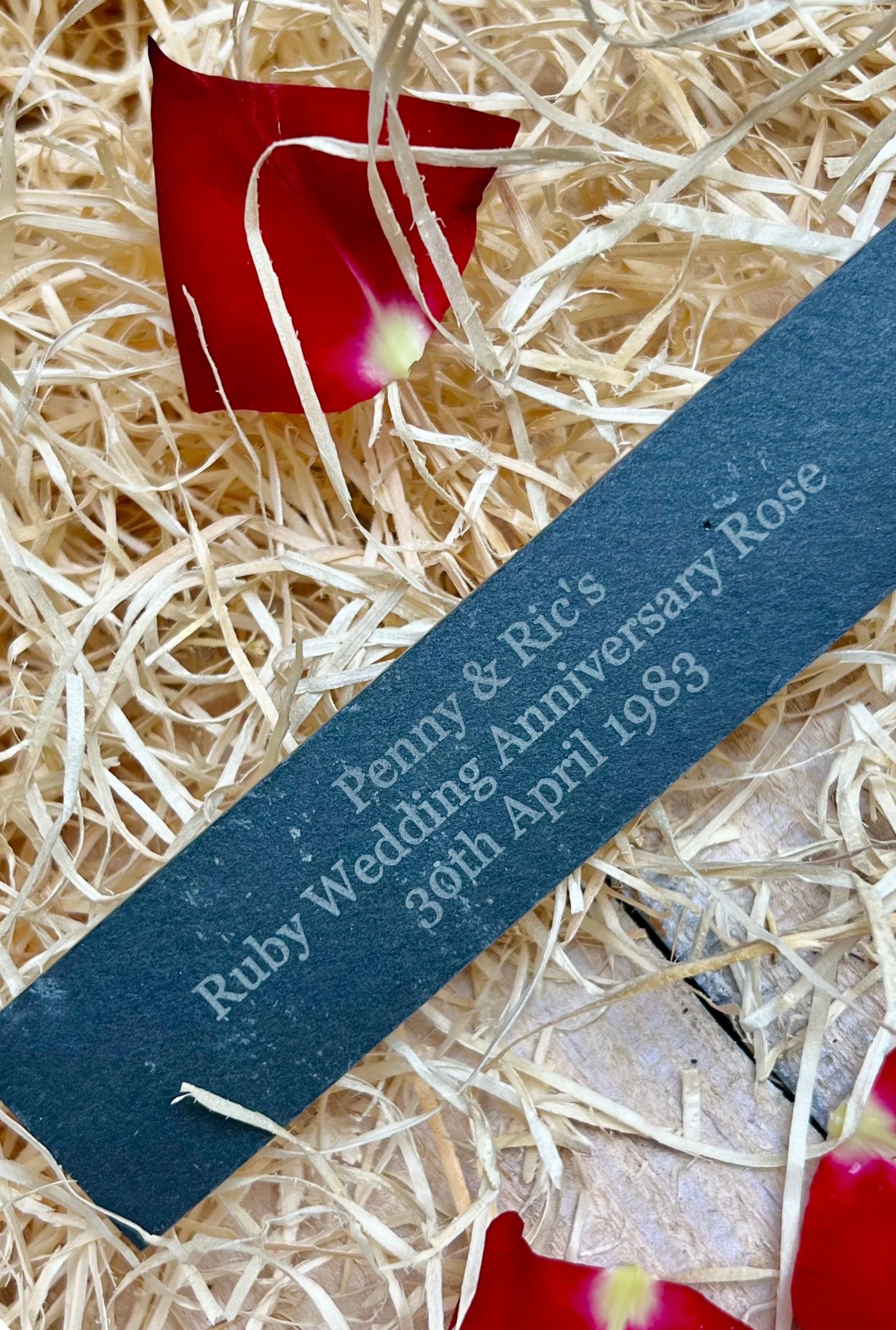 Ruby Wedding Anniversary engraved slate lying in packing straw with red rose petals.