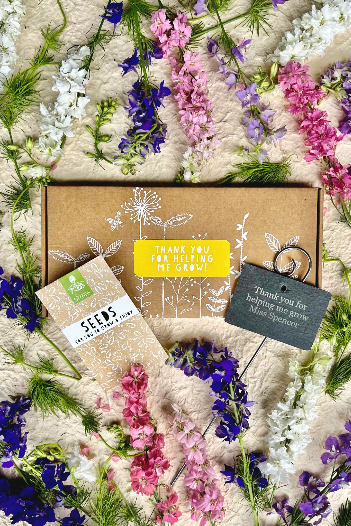 Thank You seed box with personalised slate and seed packets against white background and vibrant flowers.