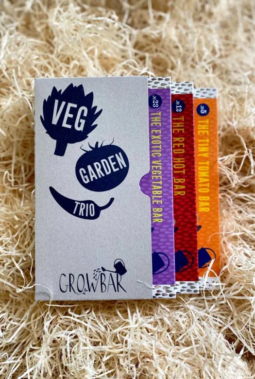 A veg garden trio box containing three different growbars in red, purple and orange colour, nestled in wood wool.