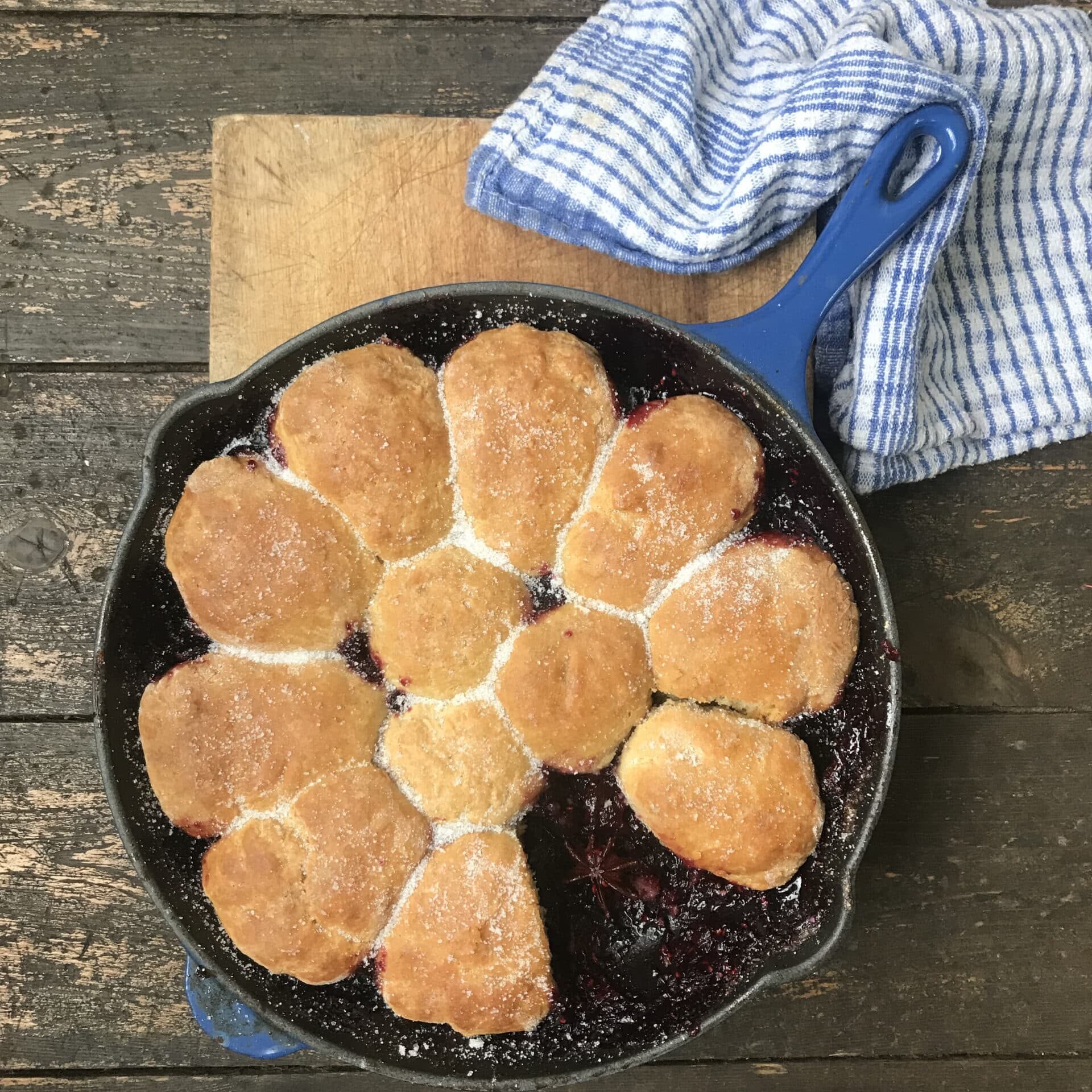 A large bowl with blackberry grunt, made of a juicy blackberry base and pastry on top sprinkled with sugar.
