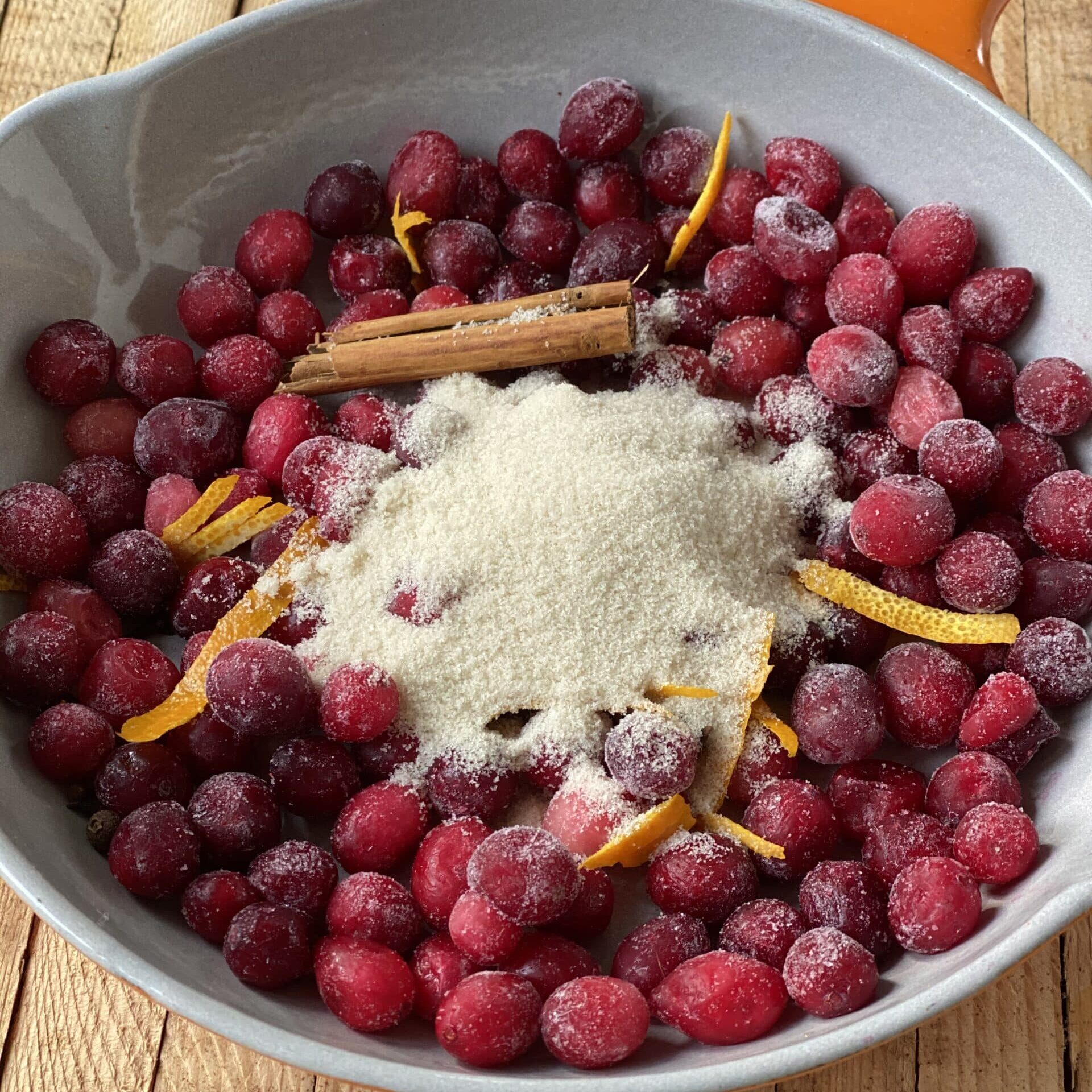 a small white dish on a wooden table with a red spiced cranberry and calamondin orange compote.