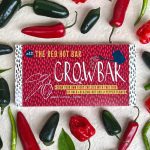 A red grow bar surrounded by an arrangement of habanero chillies, jalapeno chillies and serrano chillies and green leaves.