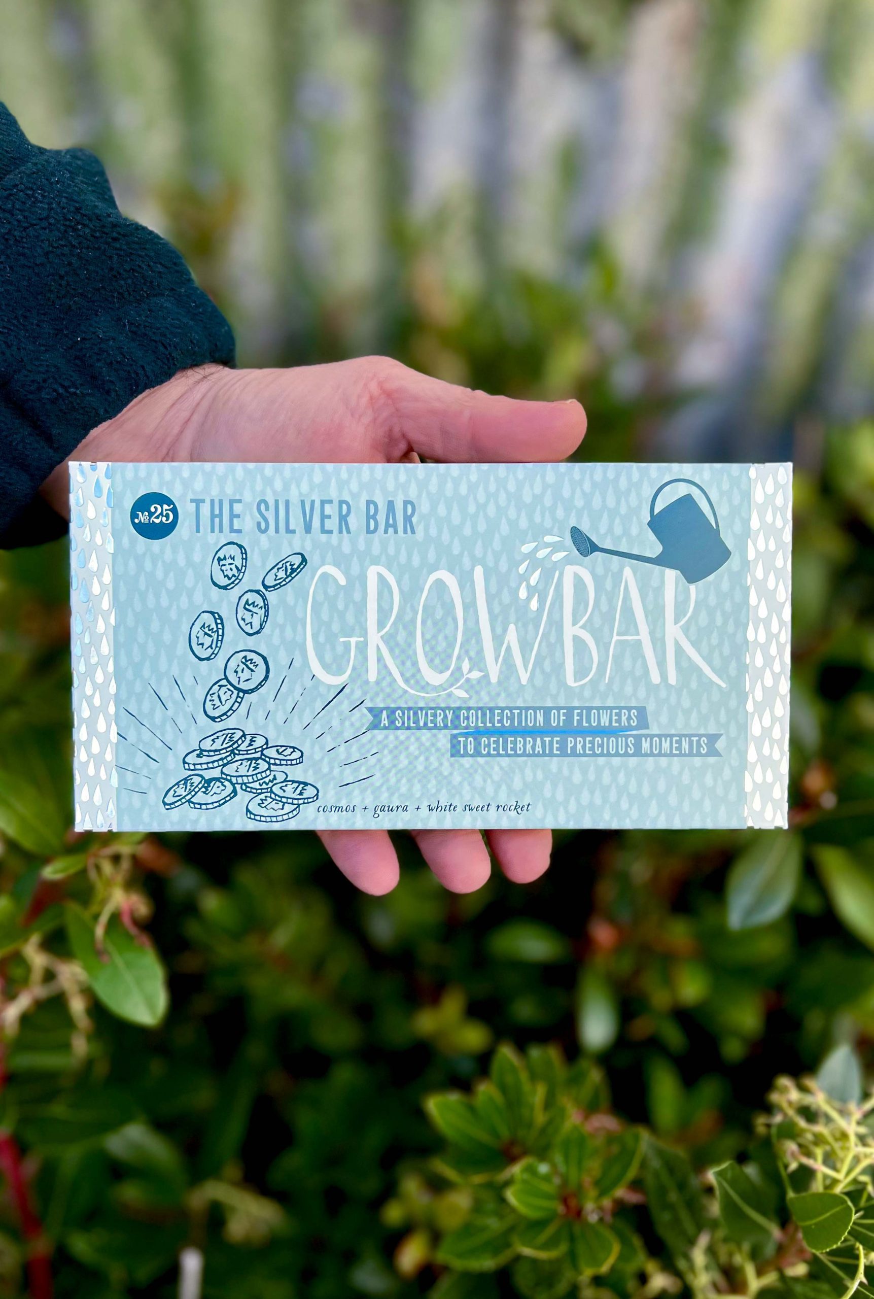 a pale blue decorative grow bar package with an illustration of coins held by a hand in front of green foliage.