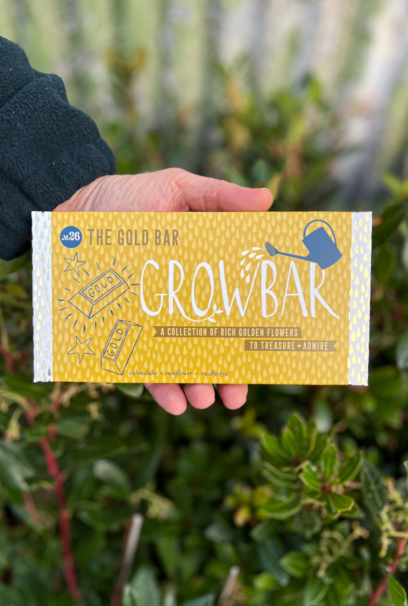 A golden-yellow Growbar package illustrated with gold bars and stars, held by a hand in front of green foliage.