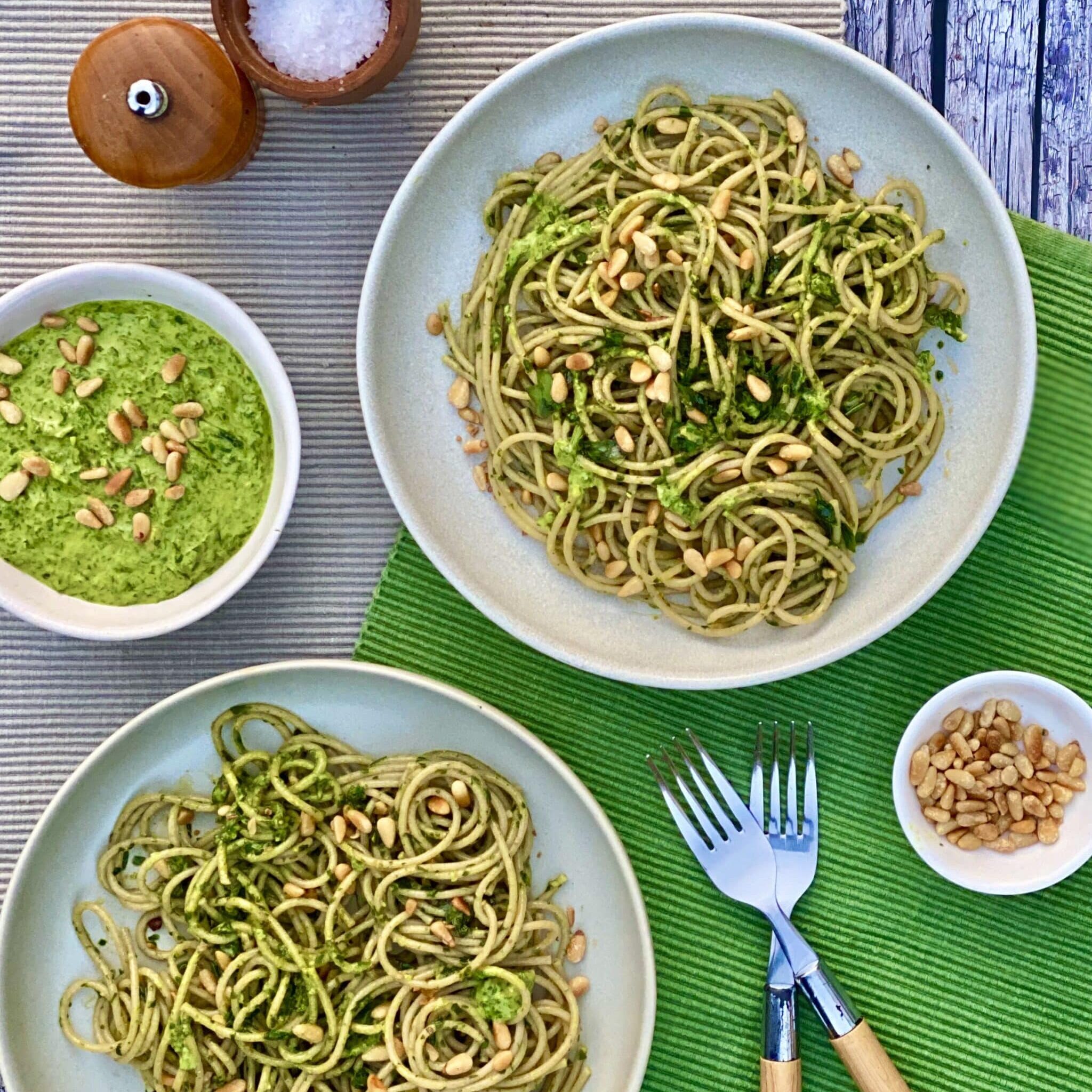Bowl of pesto with pine nuts and wooden spoon on striped background.