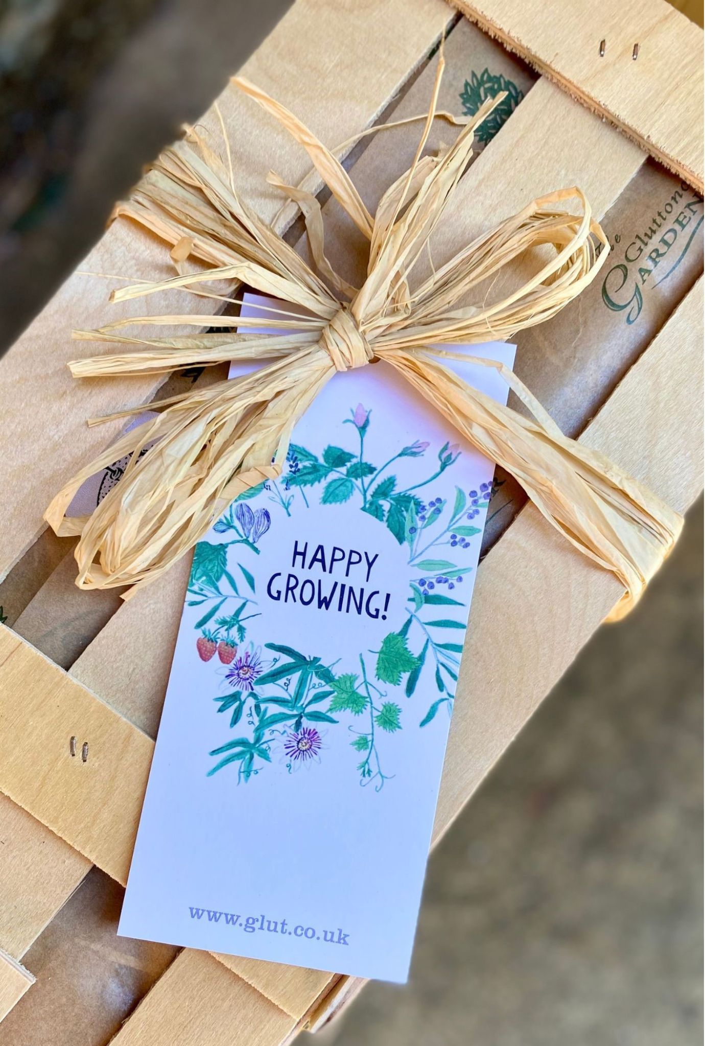 Close up of a Happy Growing gift label attached to a wooden crate with twine.