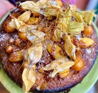 A golden brown Hazelnut and Toffee Apple Christmas Cake on a light green plate being held by two hands.