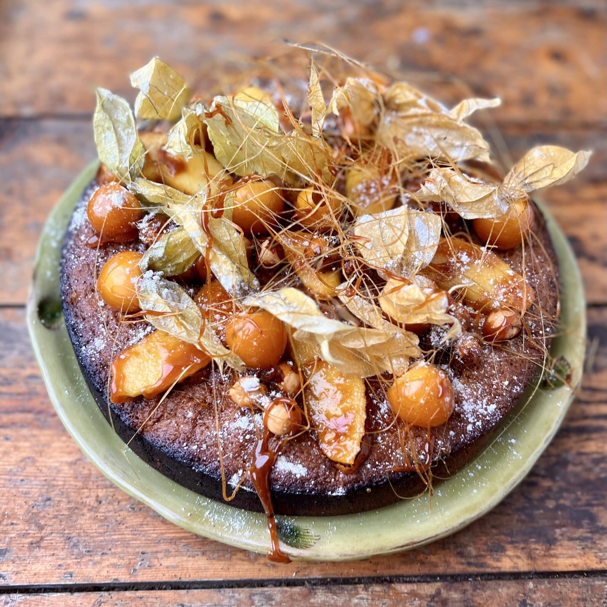 A golden brown Hazelnut and Toffee Apple Christmas Cake on a light green plate being held by two hands.